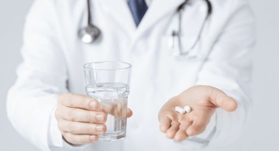 Таблетки и стакан воды в руках врача